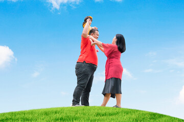 Wall Mural - Happy Asian family playing on the green hill with blue sky background