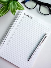 Wall Mural - To do list. Text and checklist with empty checkboxes on blank notepad page with pen, glasses and green leaves in pot on white background, vertical style. Business goals plan, resolutions concepts.