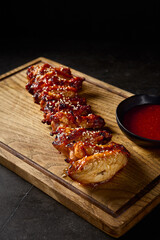 Wall Mural - Vertical close-up from the side showcasing the succulent Buffalo grilled chicken wings, sesame seeds, alongside tomato sauce, on a minimalist wooden board