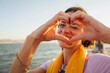 © Westend61 - Smiling woman gesturing heart shape at the waterfront