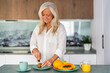 © Westend61 - Smiling woman cutting kiwi fruit and making breakfast at home