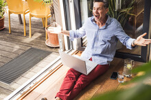 Portrait Of Happy Man Using Laptop By Open Balcony