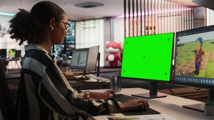 Fototapete - Female Black Game Designer Using Desktop Computer With Green Screen Chromakey on Display, Designing Characters In 3D modelling Software For RPG Video Game. Woman Working In Game Development Office