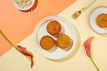 Background with coral and beige color featured two dishes of mooncakes and a dish of pumpkin seeds. Mid-Autumn Festival gradually becomes a family holiday