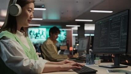 Aufkleber - Female Asian Game Programmer Coding On Desktop Computer In Game Design Studio Diverse Office. Woman Listening to Music, Writes Lines Of Code. Gameplay Engineer of New Immersive 3D Survival Video Game.