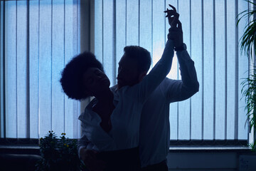 Wall Mural - dark silhouette of businessman holding hand and embracing african american woman in night office