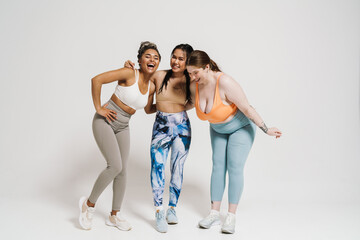 Wall Mural - Three joyful women hugging while standing isolated over white wall