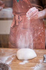 Male baker's hands working bread dough with flour on a wooden ta