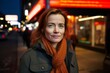 Portrait of a red-haired woman in a coat and scarf in the city at night