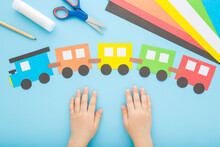 Child Hands And Colorful Paper Train With Wagons On Light Blue Table Background. Pastel Color. Point Of View Shot. Closeup. Top Down View.