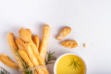 Italian Mediterranean Grissini Bread Sticks, With Aromatic Oil And Sprigs Of Rosemary, On A White Kitchen Table Background