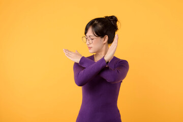 Portrait Asian beautiful young woman 30s unhappy wear purple shirt holding two cross arms say no X sign, studio shot isolated yellow background, female model pose reject gesture with copy space