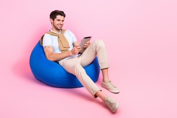 Sticker - Full body photo of peaceful cheerful man sit comfy bag use tablet empty space ad isolated on pink color background