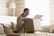 © fizkes - Laughing young woman looking into open cardboard box, unpacking parcel, sitting on couch in living room, satisfied excited customer received awaited online store order, express delivery service