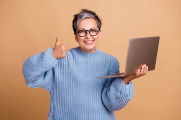 Canvas Print - Portrait of charming positive person hold netbook demonstrate thumb up isolated on beige color background