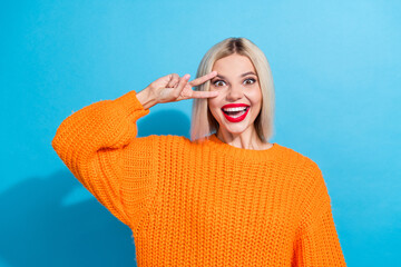 Portrait of pretty cheerful woman with bob hair dressed knitwear sweater showing v-sign on eye straing isolated on blue color background