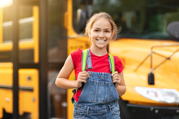 Smiling cute preteen girl standing near yellow school bus outdoors