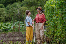 Portrait Of Grandmother With Granddaughter Hand Hoeing Soil With Hoe.