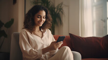 Young Adult Smiling Pretty Woman Sitting On Chair Holding Smartphone Using Cellphone Modern Technology, Looking At Mobile Phone While Remote Working Or Learning, Texting Messages At Home Office