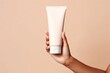 © id512 - woman hand is holding a white mockup tube of facial cream on a beige isolated background