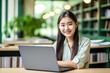 © AI_images - Happy Asian girl student using laptop computer in university library sitting at desk