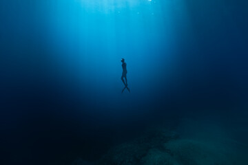 Freediver Swimming in Deep Sea With Sunrays. Young Man DIver Eploring Sea Life.