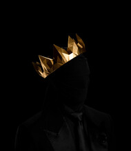 Man Dressed In Black Suit Holding Gold Objects On Black Background