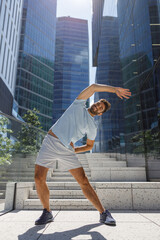 Healthy sporty man doing stretch on modern city skyscrapers background. Healthy lifestyle concept