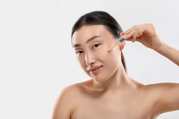 Canvas Print - Beautiful young woman applying cosmetic serum onto her face on white background, space for text