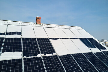 Wall Mural - Aerial view of snow melting from covered solar photovoltaic panels installed on house rooftop for producing clean electrical energy. Low effectivity of renewable electricity in nothern region winter