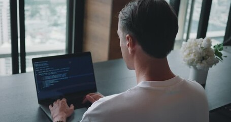 Over the shoulder, Man Programmer Working at Laptop Computer sitting at workplace in office, writing code. Back view programmer man using laptop writing program code at office table. IT start up