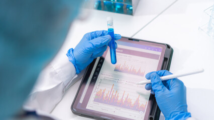 scientist in laboratory holding test tube looking at health and blood result report on digital tablet analysis chemistry hospital