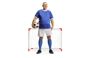 Poster - Mature man in a blue football jersey holding a ball and smiling in front of a mini goal