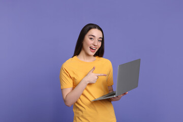 Poster - Smiling young woman with laptop on lilac background