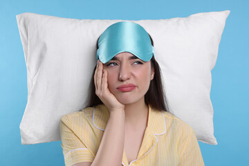 Sticker - Tired young woman with sleep mask and pillow on light blue background. Insomnia problem