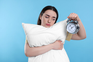 Canvas Print - Tired young woman with pillow and alarm clock on light blue background. Insomnia problem