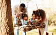 © Anela/peopleimages.com - Parents with kids in park, tree swing and freedom for love, bonding or peace in nature together. Mother, father and children adventure in garden, black family on summer weekend in woods or forrest.
