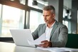 © id512 - a busy, mature male executive, holding documents and working on a laptop, while attentively viewing his computer screen at his office desk