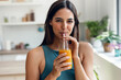 © nenetus - Beautiful sporty woman drinking healthy orange juice while standing in the kitchen at home