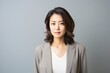 © Leon Waltz - medium shot portrait of a serious, Japanese woman in her 40s wearing a chic cardigan against a minimalist or empty room background