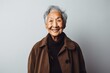 Portrait of a Mexican woman in her 90s wearing a versatile overcoat against a minimalist or empty room background