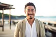 © Leon Waltz - portrait of a happy Japanese man in his 30s wearing a chic cardigan against a beach background