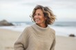 medium shot portrait of a Israeli woman in her 50s wearing a cozy sweater against a beach background