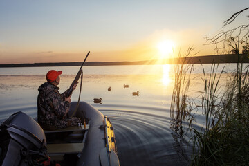 Wall Mural - The hunter with a rifle sit in an inflatable boat and looking out for something. Duck hunter at sunrise.