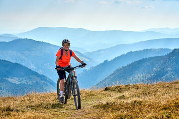 Wall Mural - nice senior woman on her electric mountain bike cycling on Feldberg summit with stunning view over the Black Forest mountains and valleys, Baden-Wuerttemberg Germany