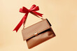 Fashion Leather Brown Bag Wrapped with a
Red Ribbon, flying at an 45 degree angle on
pastel beige color background. Trendy beauty
woman concept, fashion and holidays. Close-
up, copy space. Front view