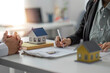 © wichayada - Agents and clients discuss contracts to buy, insure, or borrow real estate or assets. along with viewing a sample house model.