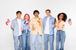 © Prostock-studio - Student exchange, language learning. Happy multiracial friends in casual, holding small flags of different countries