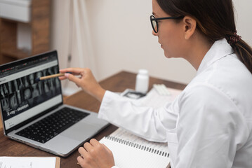 Aufkleber - Young doctor in glasses looks at X-ray images pointing with pencil at laptop screen female traumatologist diagnoses patient working with examination results side view