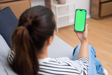 Poster - Woman chats in social networks on phone sitting on sofa closeup female relaxes at home looking at smartphone screen with chromakey backside view on blurred background